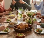 אווירת אירוח: קנקן זכוכית אלגנטי מלא במים צוננים המוגש לצד צלחות עמוסות ומשפחה סועדת.