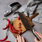 סכין שף אוריינטלית Global G-4 על קרש חיתוך, לצד בשר וירקות.