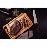 סכין חדה של טרמונטינה ליד סטייק עסיסי על קרש חיתוך, מדגימה מוכנות לחיתוך מדויק.