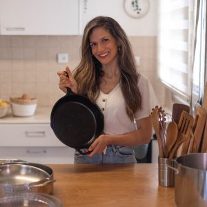 מיכל מורו אקרמן מציגה מחבת ברזל יצוק של Lodge מומלצת, על רקע מטבח מעץ וכלים