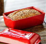 אופה לחם Emile Henry פתוח, כשהמכסה מונח הפוך על השיש, המדגים את ידיות האחיזה הנוחות ואת אפשרות האחסון החסכונית במקום.