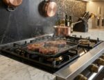 פלנצ'ת פסים Swiss Diamond מונחת על כיריים גז ועליה נתחי סטייק עסיסיים בתהליך צלייה