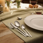 שולחן אוכל מעוצב עם סט סכו"ם Salvinelli 250 Ice על מפת שולחן ירוקה זית לצד צלחת לבנה.