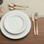 שולחן אירוח מודרני עם סכו"ם Salvinelli Fast Ice Copper, צלחות לבנות מעוטרות ויין אדום.