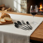 שולחן אירוח מודרני עם סכו"ם Salvinelli Fast Ice Black, לחם כפרי, כוס יין אדום ואווירת אח בוערת ברקע.