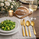 שולחן אירוח חגיגי עם סכו"ם Salvinelli Fast Ice Gold, צלחת לבנה עם סלט ירוק וכוס יין לבן.