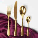 מבט על סימטרי: סט סכו"ם Salvinelli Forever Gold בציפוי זהב מסודר על מפית בד בהירה ויוקרתית.