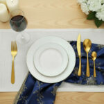 שולחן אירוח חגיגי עם סכו"ם Salvinelli Forever Gold, צלחת לבנה עם סלט ירוק וכוס יין לבן.