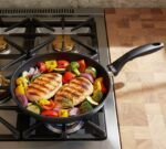 חזה עוף צרוב וירקות צבעוניים מתבשלים על כיריים בתוך מחבת Swiss Diamond 26 ס"מ עם ציפוי יהלומים.