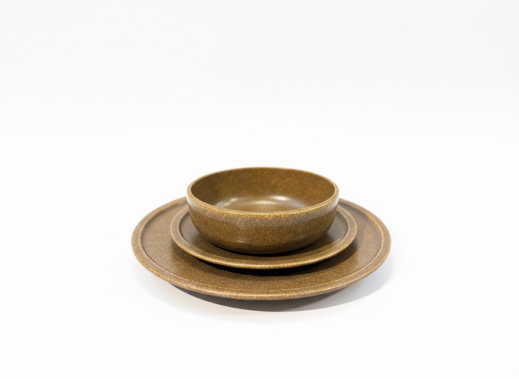 שלושה כלי הגשה מפורצלן בצבע חום-דבש מדורגים: צלחת שטוחה גדולה, מעליה צלחת בינונית ובחלק העליון קערה עמוקה, מוצגים על רקע לבן חלק מערכת אוכל יוקרתית מפורצלן RAK דגם IZE בגוון דבש, צילום תקריב על רקע לבן המדגיש את המרקם האיכותי והעיצוב המודרני של הסט